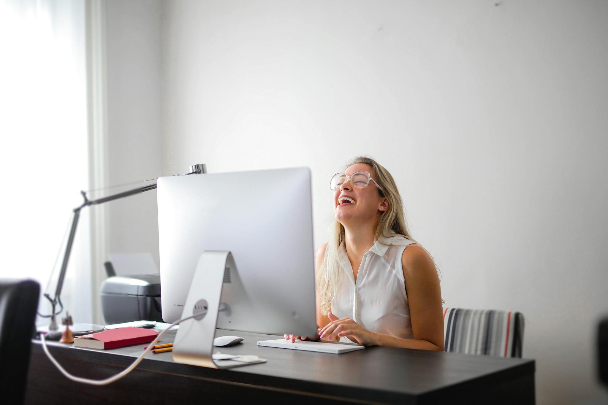 Woman in White Tank Top Using Macbook Air on Brown Wooden Table