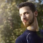 Handsome guy in sportswear and with earring standing in park in sunny summer day and looking away